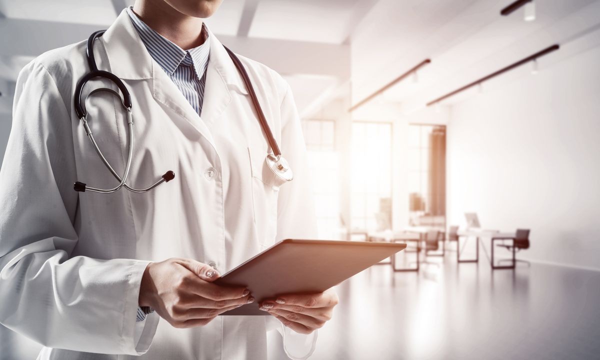 Close up of successful female doctor standing with tablet in hands indoors of white medical office building. Young woman doctor. Medical industry concept